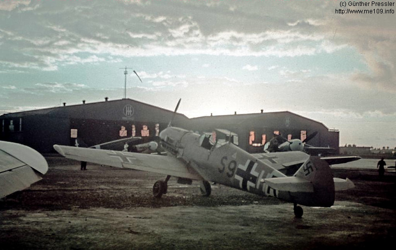 Bf 109 E-7/Trop, Lt. Kurt Pressler, Schlachtgeschwader 1, I. Gruppe, Deutschland, S9+HR, Die Aufnahme entstand in Italien, wie die Hoheitszeichen an den Flugzeughalle…